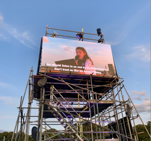 A young person at the top of scaffolding tower in Roundhay park Leeds reads speeches